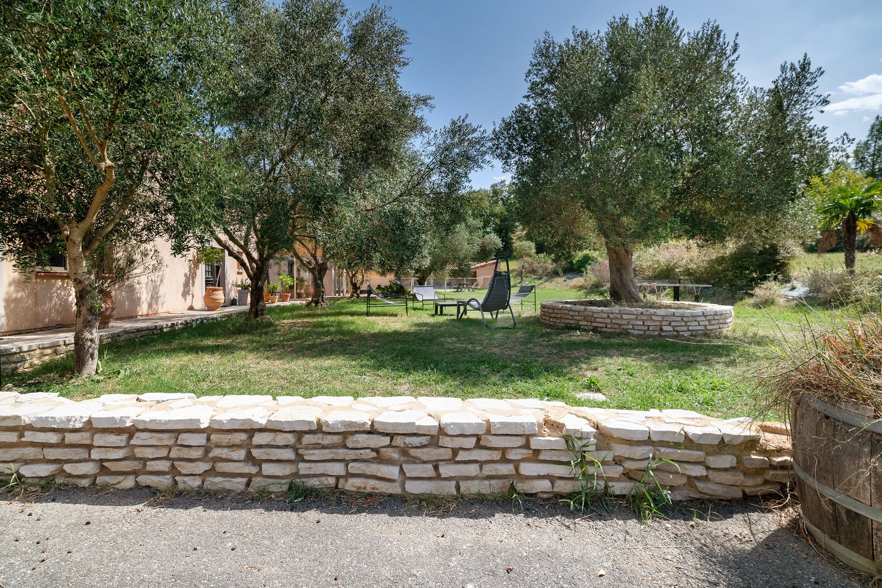 Une cour bordée de murs en pierre, avec des espaces de repos en plein air et des oliviers.