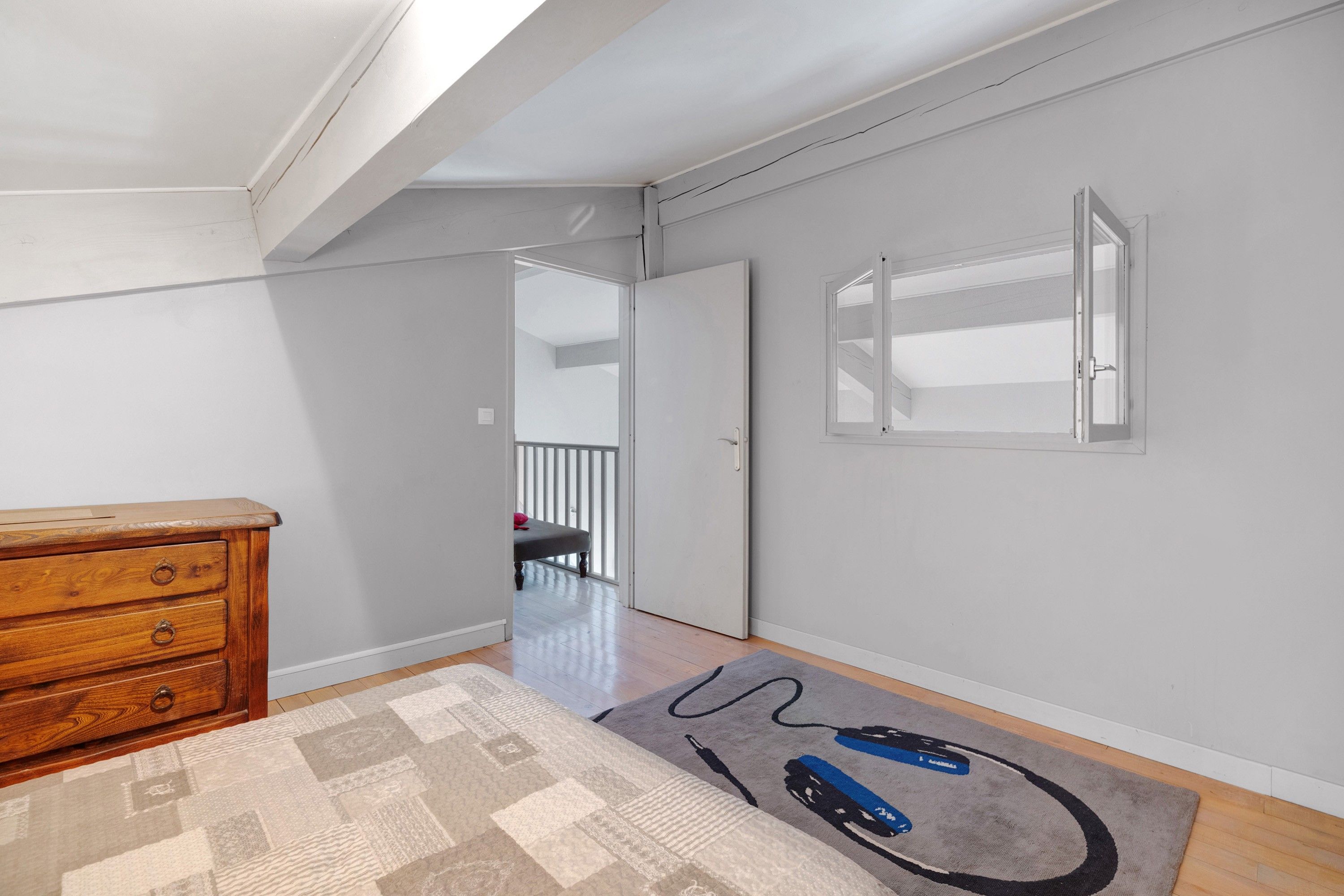 A room with a wooden dresser, a patterned rug, and a door leading to another room.