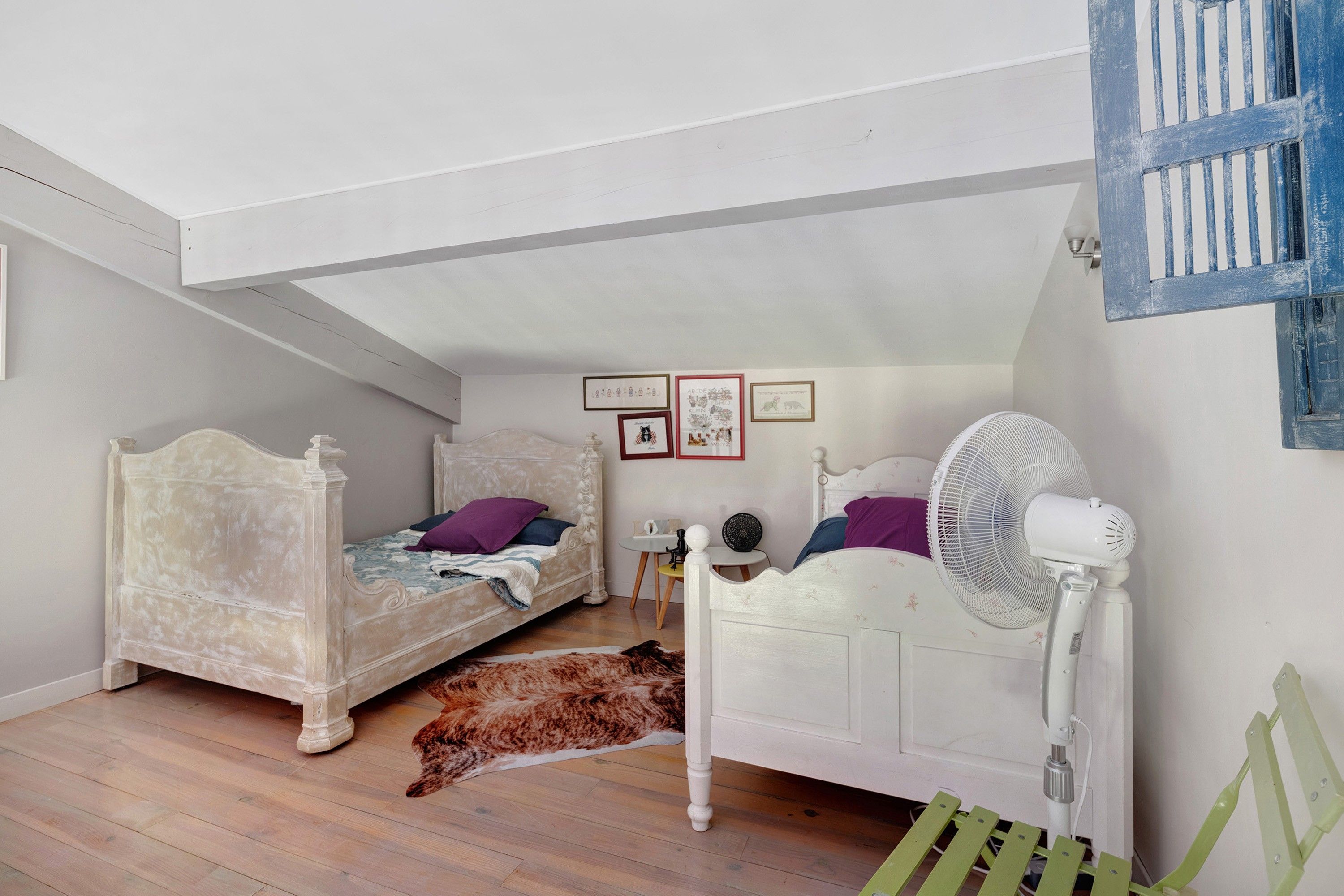 Un dormitorio con dos camas, un ventilador, una alfombra y decoración en la pared.