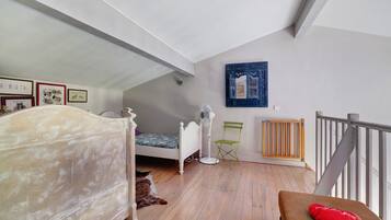 Un dormitorio con una cama, un ventilador de pie, un radiador y una silla plegable verde.
