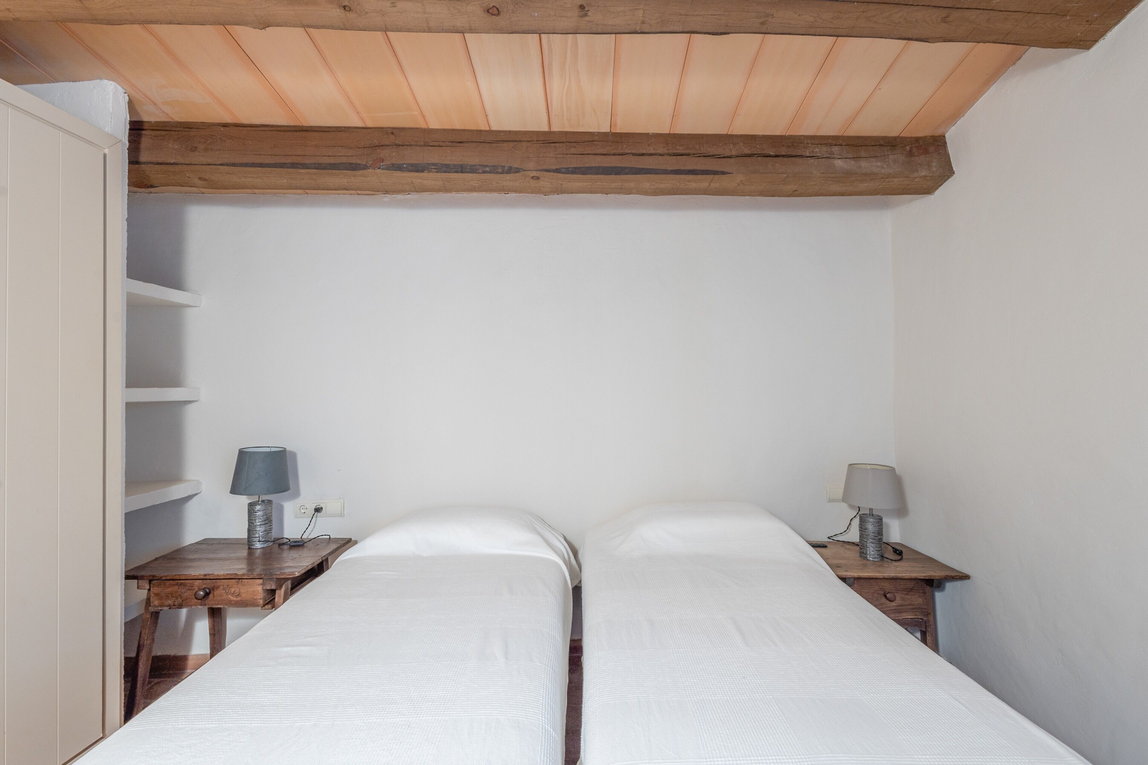 Una habitación pequeña y sencilla con dos camas individuales, mesitas de noche de madera y techo inclinado.