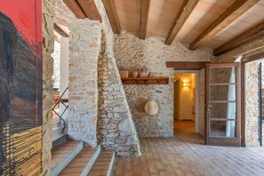 A stone interior with a wooden staircase, a shelf with baskets, and a door leading to another room.