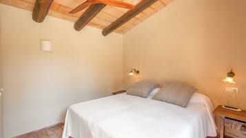 Un dormitorio con una cama, dos lámparas de noche, techo de madera y piso de baldosas.