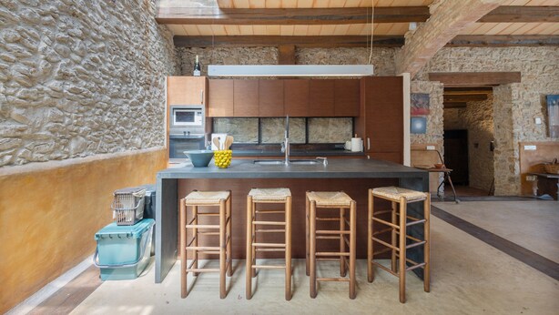 Una cucina con isola centrale, sgabelli di legno e parete in pietra.