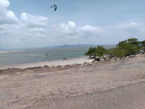 Une plage où l’on pratique le kitesurf, une mer calme et des montagnes à l’horizon.
