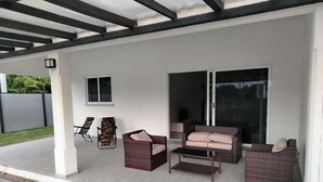 Een overdekt terras met buitenmeubilair, een schuifpui en een klein raam.