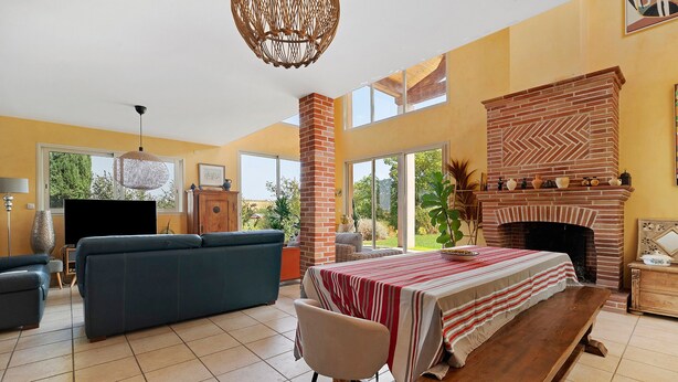 Un salón amplio con sofá, una mesa de comedor con mantel a rayas rojas y blancas, chimenea y televisor.
