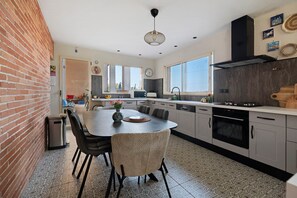 A modern kitchen with a central island, dining chairs, a built-in oven, and a large window providing natural light.