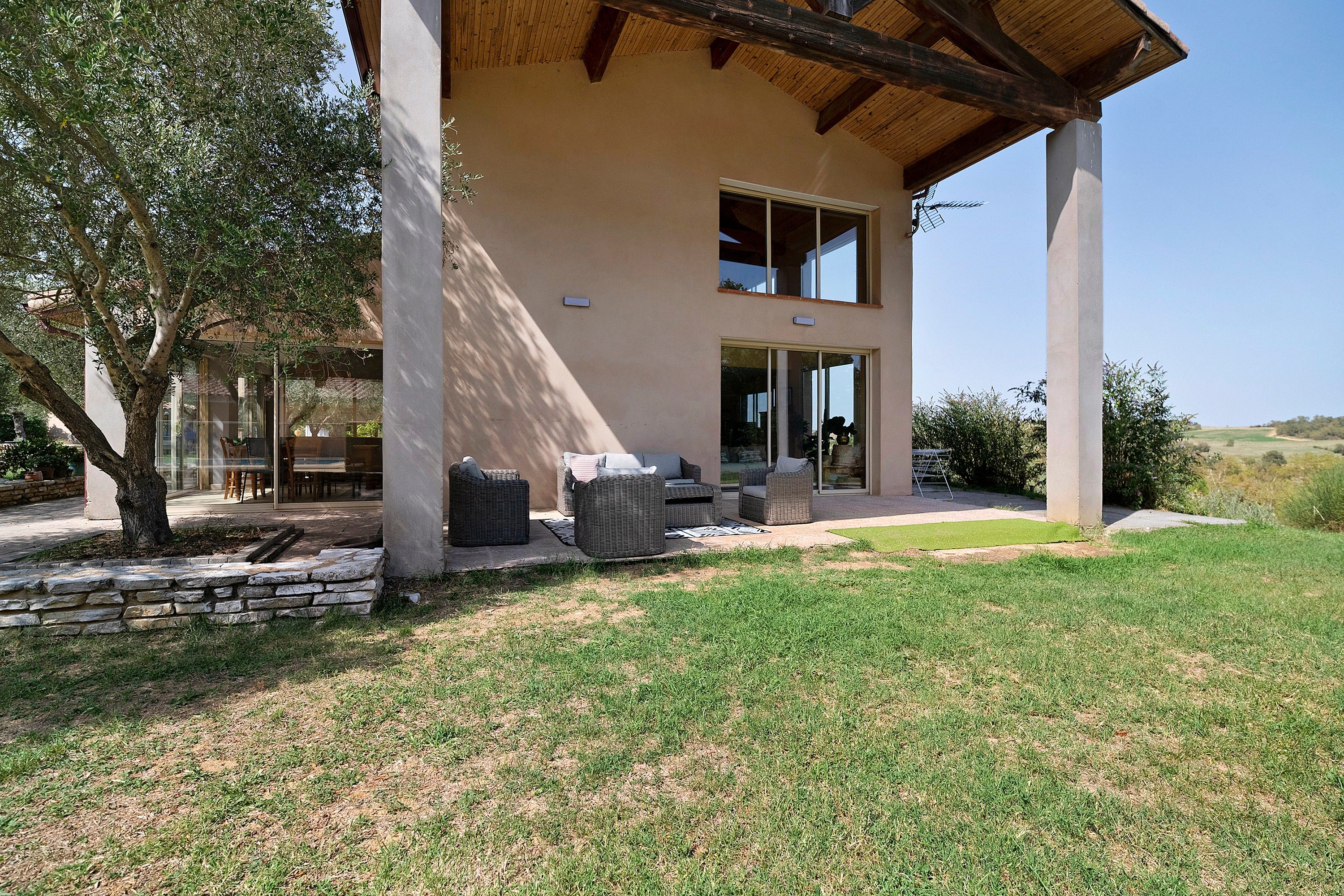 Une maison moderne dotée d’un patio couvert, d’un espace salon extérieur et d’un mur en pierre.