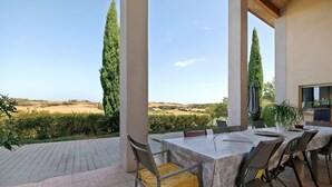 Un patio exterior con mesa y sillas, con vistas a un paisaje rural con campos y árboles.