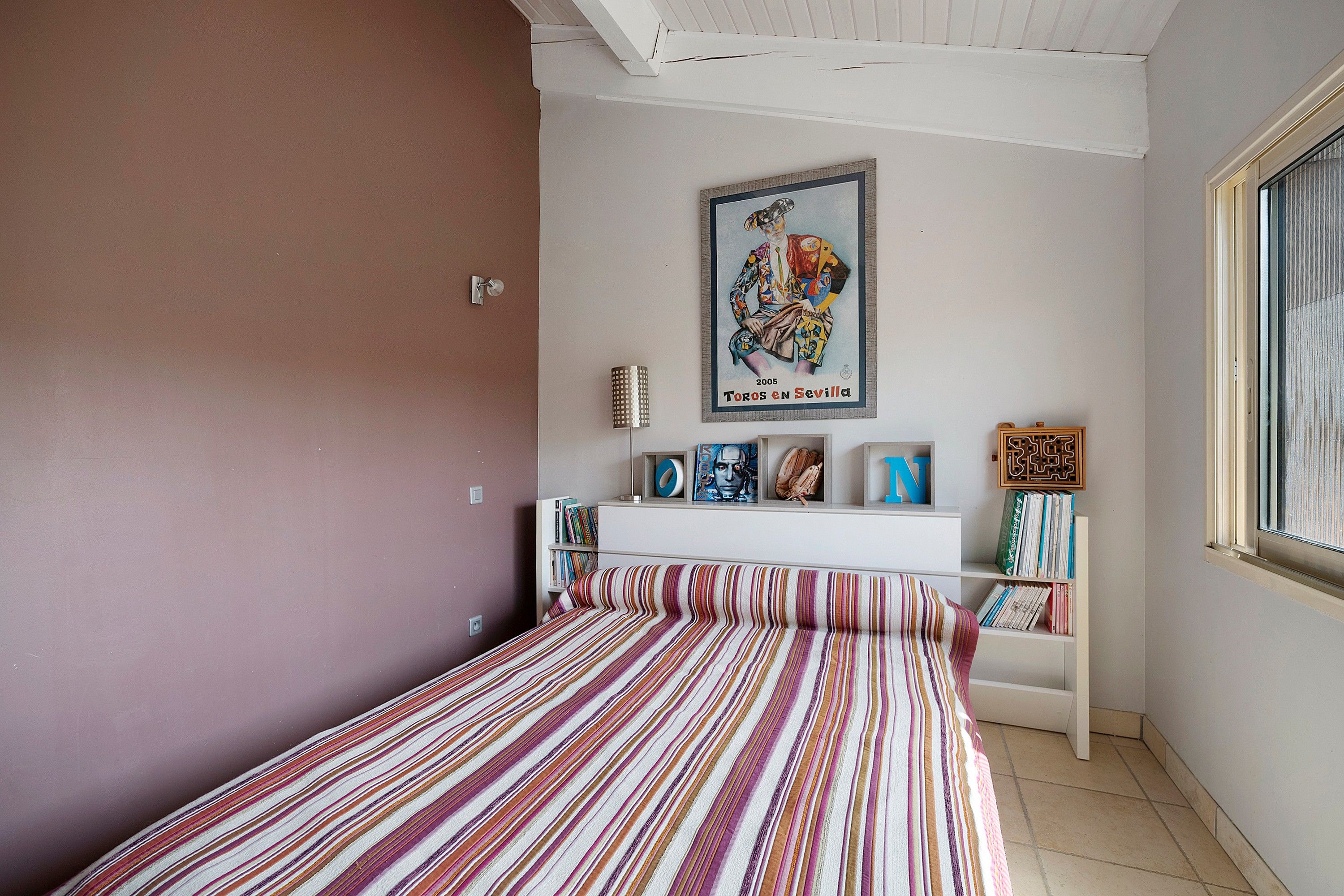 A bedroom with a striped bedspread, a white dresser, and a framed poster on the wall.