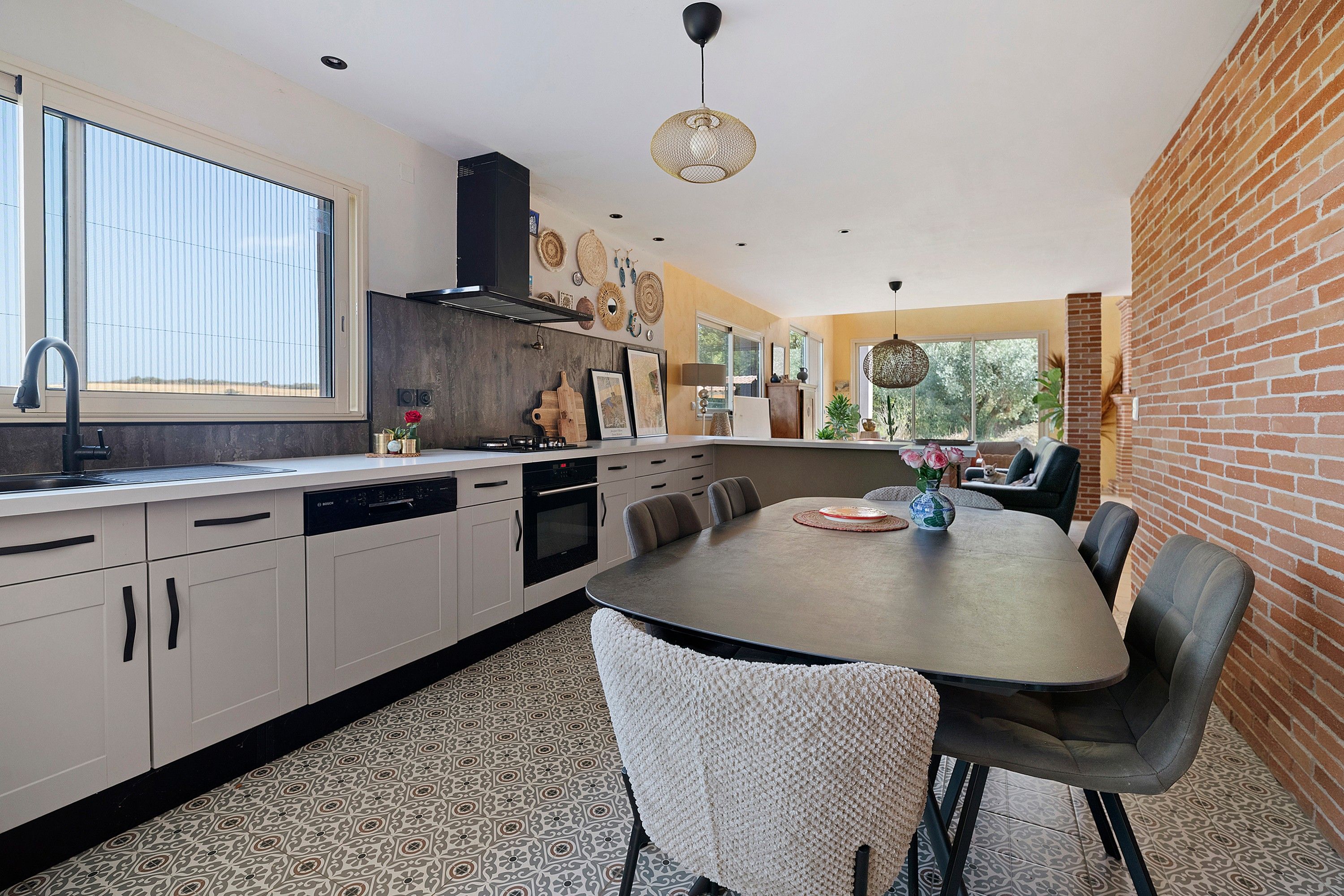 Une cuisine moderne avec un coin repas, comprenant un grand îlot central, des appareils électroménagers intégrés et un mur décoratif en briques.