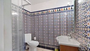 Un baño con pared de azulejos, inodoro, lavamanos y zona de ducha.