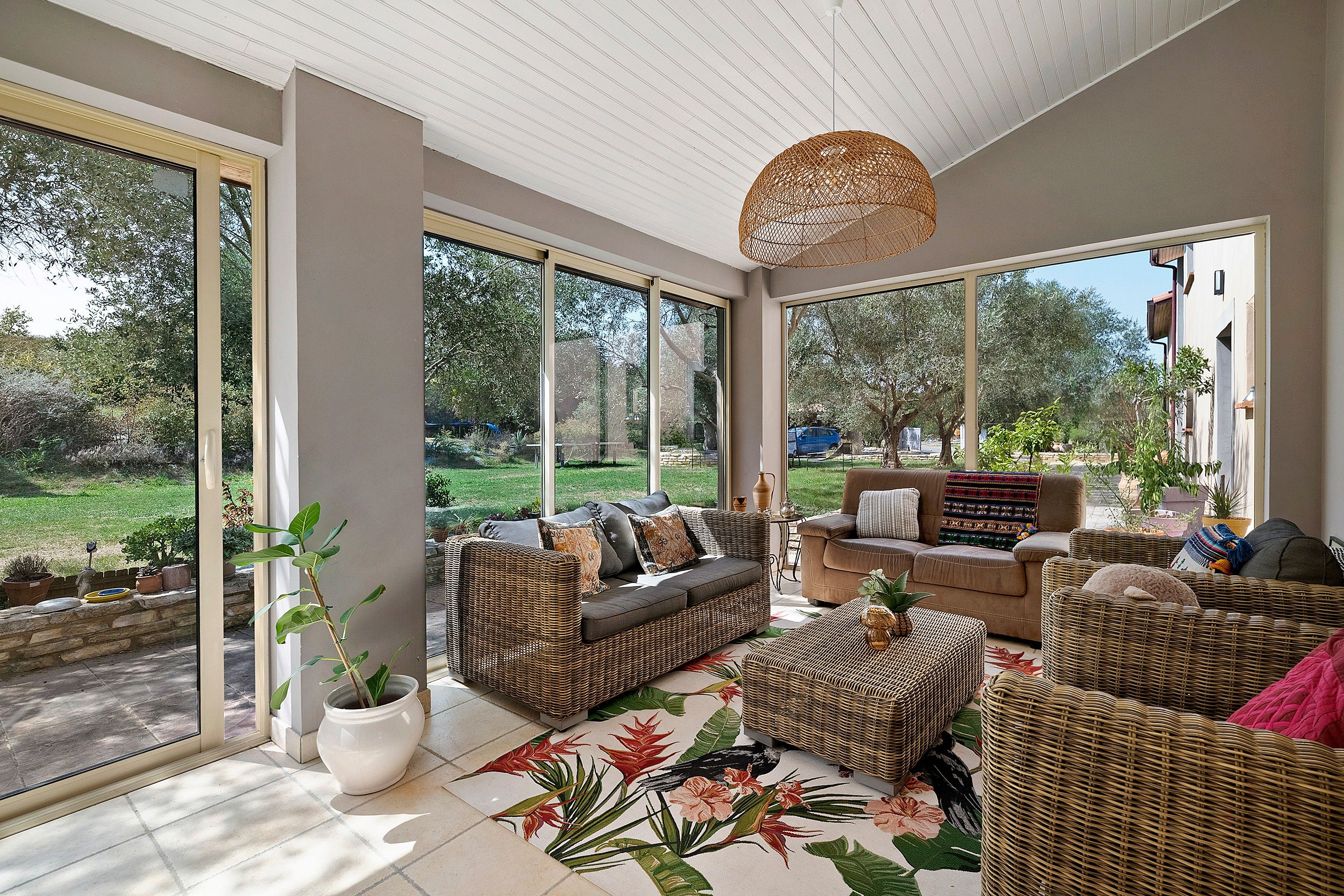 A sunlit room with large windows, wicker furniture, and a view of a garden.