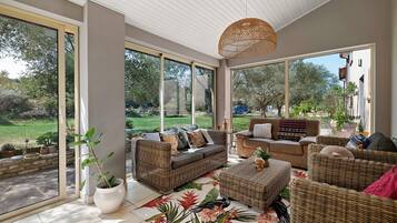 A sunlit room with large windows, wicker furniture, and a view of a garden.
