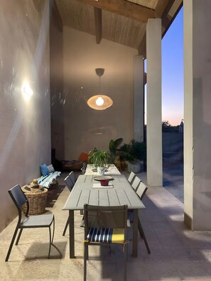 An outdoor dining area with a long table, chairs, and a hanging light fixture.