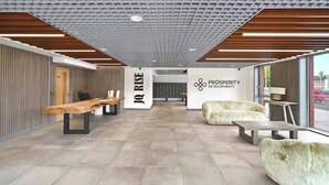 Ein moderner Empfangsbereich mit hohen Decken, Holzbalken und einer zentralen Wand mit dem Logo 'IQ RISE' und 'PROSPERITY & DEVELOPMENTS'.