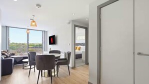 Ein modernes Wohnzimmer mit Essbereich, einem an der Wand befestigten Fernseher und Blick auf die Stadt.