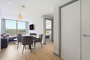 A modern living room with a dining area, a TV mounted on the wall, and a view of the cityscape. - Apartment Sleeps 4 - Air Con, City Centre, Wifi (Birmingham)