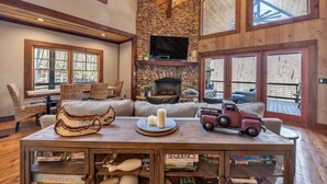 A cozy living room with a stone fireplace, wooden furniture, and a television mounted above it. - Blue Ridge Escape | Luxury Mtn. Cabin near Lake BR (Blue Ridge)