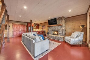 A cozy living room with a stone fireplace, a sofa, and a patterned armchair. - Blue Ridge Escape | Luxury Mtn. Cabin near Lake BR (Blue Ridge)