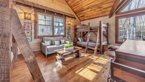 A cabin interior with a wooden ceiling, bunk beds, a sofa, and a dining table. - Blue Ridge Escape | Luxury Mtn. Cabin near Lake BR (Blue Ridge)