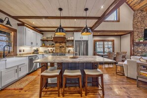 A spacious kitchen with a large island, wooden bar stools, and a stone fireplace. - Blue Ridge Escape | Luxury Mtn. Cabin near Lake BR (Blue Ridge)