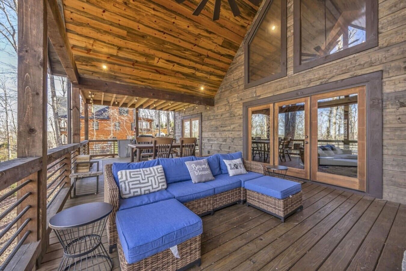 A covered outdoor seating area with a wooden deck, wicker furniture, and a view of the surrounding landscape.