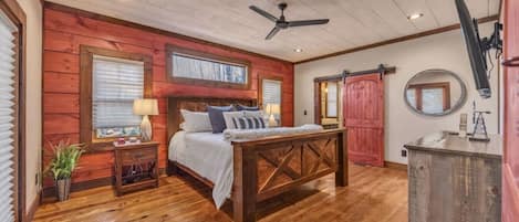 A bedroom with a wooden ceiling, a bed with pillows, a nightstand, a desk, and a red door.
