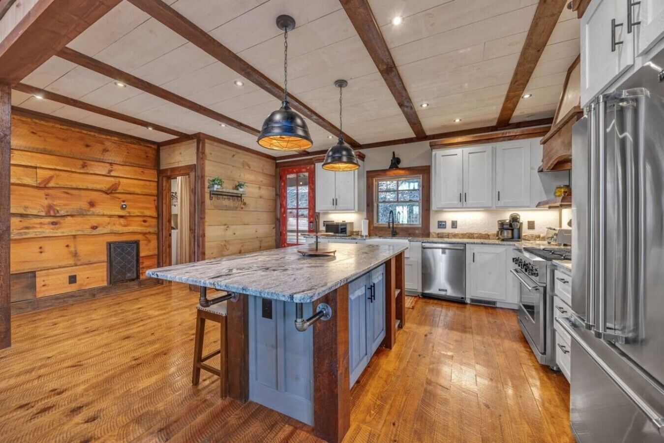 A kitchen with wooden walls, a central island, stainless steel appliances, and pendant lighting.