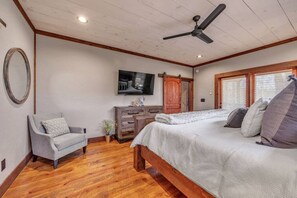 Ein Schlafzimmer mit einem Bett, einem Sessel, einem Fernseher, einer Kommode und einem Deckenventilator.