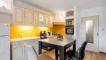 Een keuken met witte kasten, een gele achterwand, een eettafel met stoelen en een deur met een handgreep.