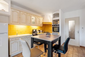 Una cocina con armarios blancos, un salpicadero amarillo, una mesa de comedor con sillas y una puerta con pomo.
