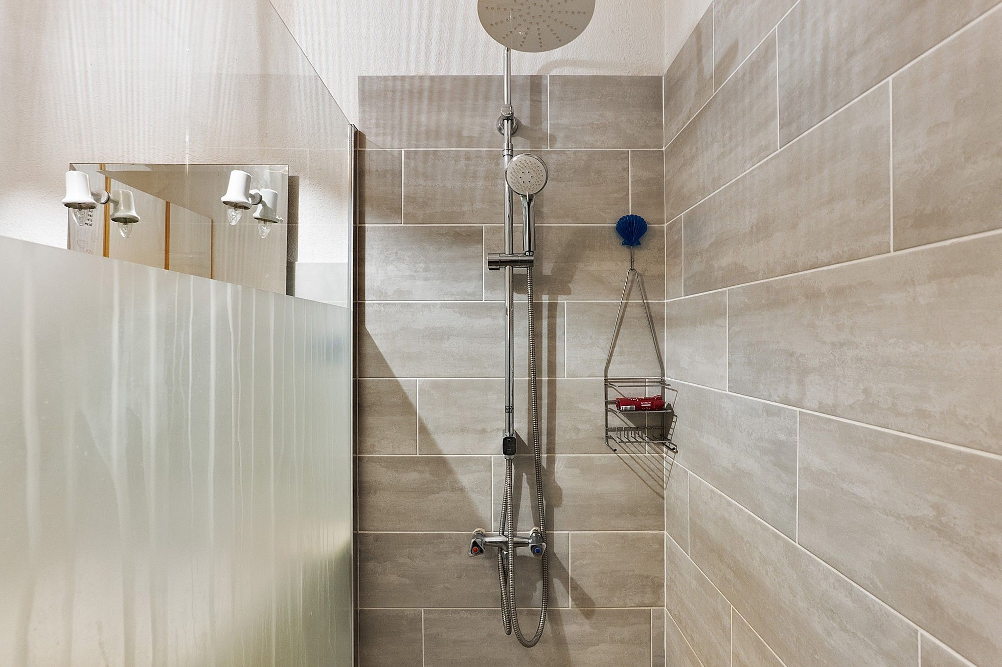 A modern shower with a handheld showerhead, a wall-mounted faucet, and a handheld showerhead with a blue scrubber.