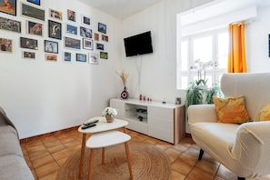 A living room with a sofa, a coffee table, a flat-screen TV mounted on the wall, and a window with curtains. - Chez Géraldine Apartment (Sainte-Croix-du-Verdon)