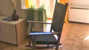 A room with a rocking chair, a small table with a vase, and a window with curtains. - Chez Géraldine Apartment (Sainte-Croix-du-Verdon)