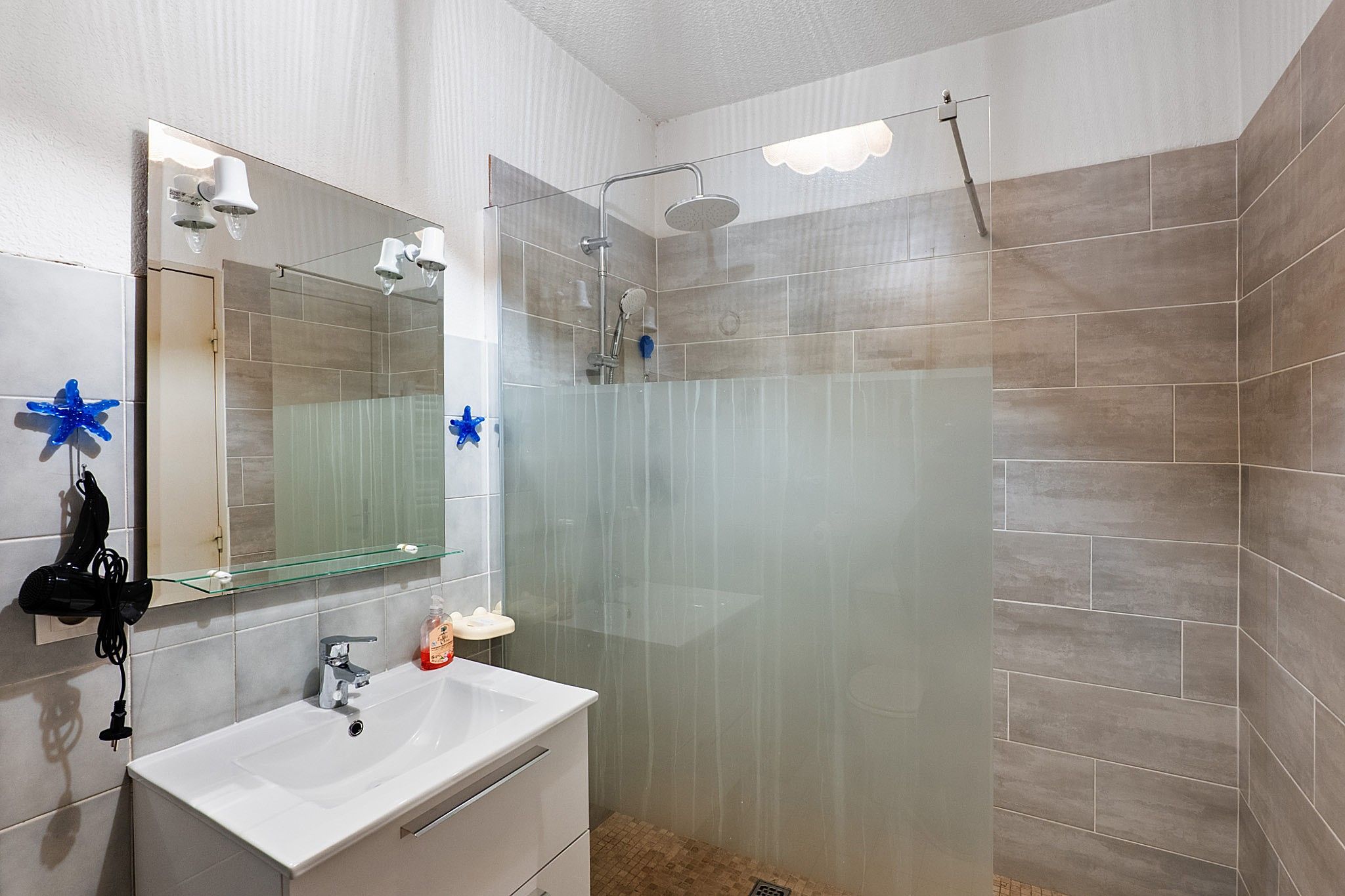 Une salle de bain avec une douche à parois de verre, un lavabo blanc et un miroir avec éclairage intégré.