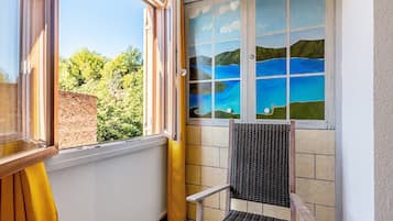 Ett rum med utsikt över en sjö genom ett fönster, en stol och en gul gardin.