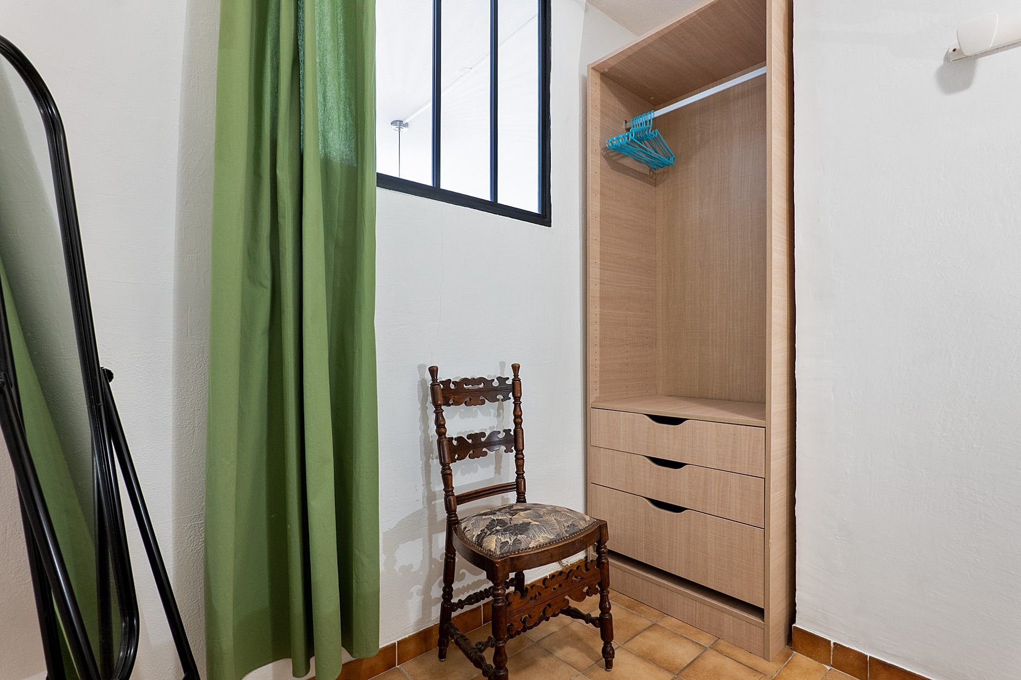 A room with a wooden chair, a wooden wardrobe, and a green curtain.