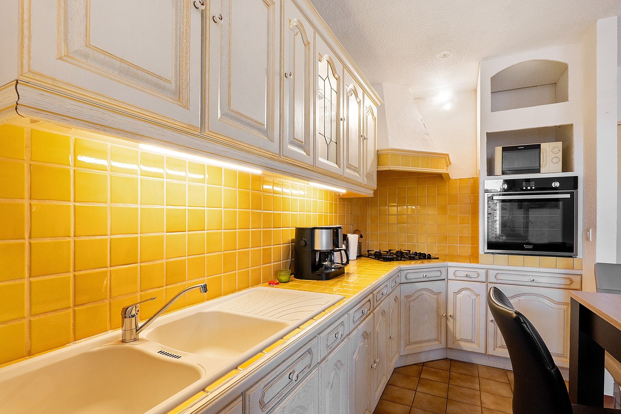 Una cocina con azulejos amarillos, un fregadero, una estufa y un microondas.