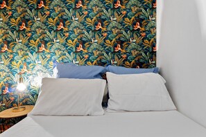 Una cama con ropa blanca, dos almohadas y una mesita de noche con una lámpara.