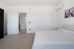 Un dormitorio con cama, una puerta, un equipo de aire acondicionado y un cuadro en la pared.