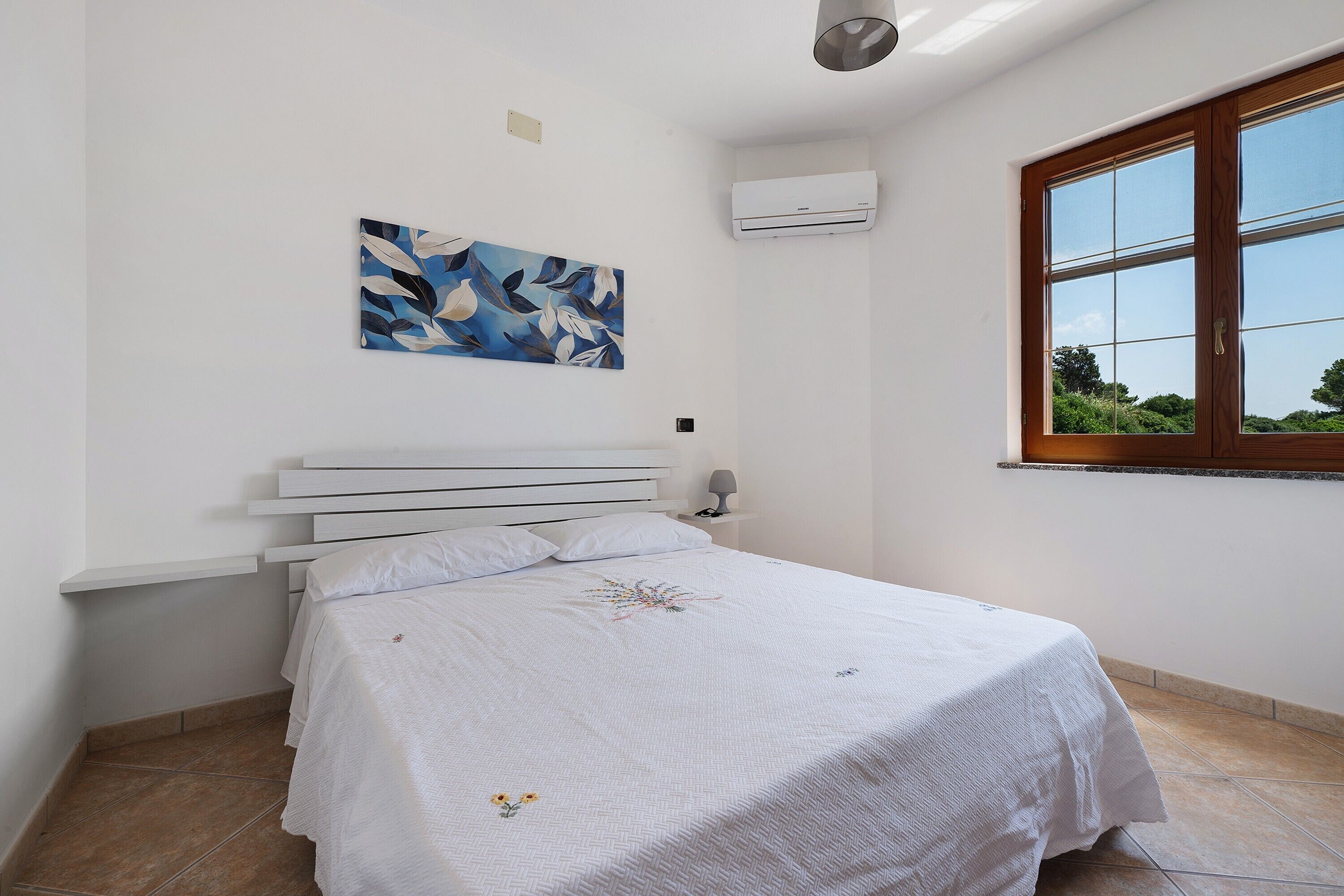 Una camera da letto con un letto, un condizionatore d'aria a parete, una finestra con vista e un quadro appeso al muro.