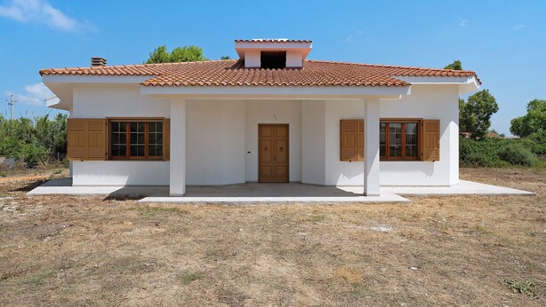 Ein einstöckiges Haus mit Ziegeldach, einer mittleren Tür und je zwei Fenstern auf jeder Seite.