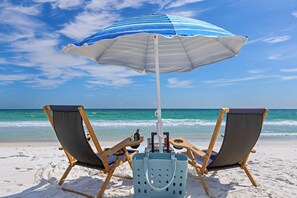 A beach scene with two wooden beach chairs and a blue and white striped umbrella. - Suncerre- 100 Steps to Private Beach & Pool in Carillon Beach (Panama City Beach)