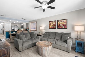 A modern living room with a grey sectional sofa, a round coffee table, and a ceiling fan. - Dog Friendly Condo with Gulf Views (Miramar Beach)