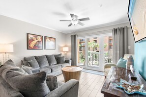A modern living room with a grey sofa, a round wooden coffee table, and a ceiling fan. - Dog Friendly Condo with Gulf Views (Miramar Beach)