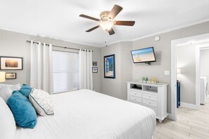 Ein Schlafzimmer mit Bett, Deckenventilator, Fernseher und Kommode.