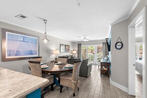 A dining area with a round table, wicker chairs, and a ceiling fan. - Dog Friendly Condo with Gulf Views (Miramar Beach)