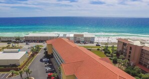 A hotel with a red-tiled roof, a parking lot, and a view of the ocean. - Dog Friendly Condo with Gulf Views (Miramar Beach)